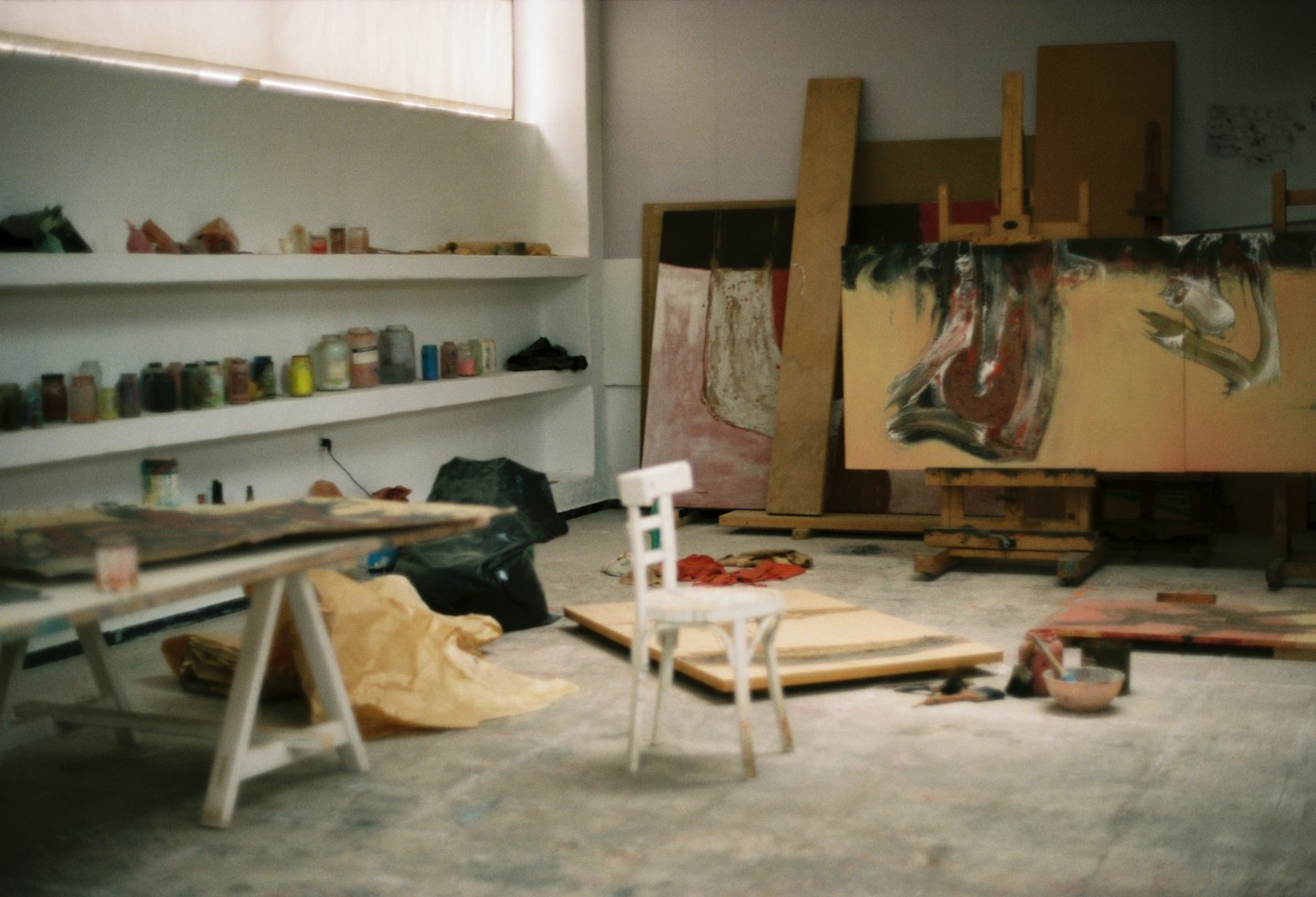 Artist's studio with canvases on easels and art supplies on shelves.