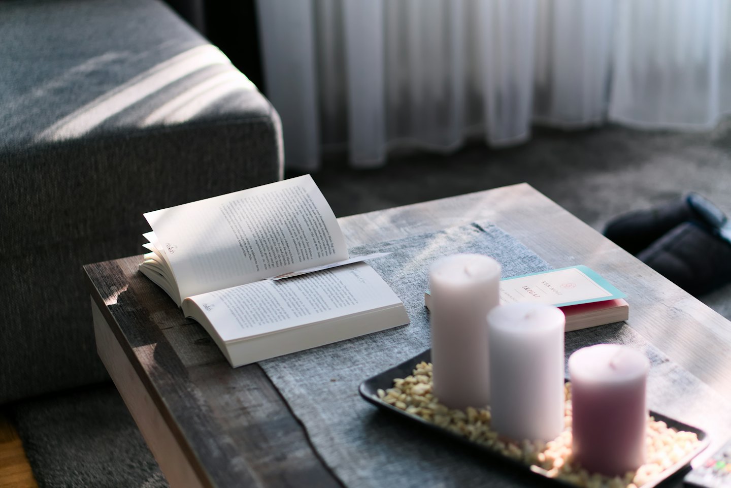 Open book and candles sitting on a wooden coffee table.